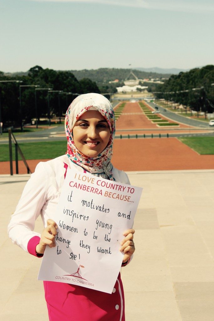 Young woman wearing a hijab holding a sign which states "I love country to canberra because... it motivates and inspires young women to be the change they want to see!"